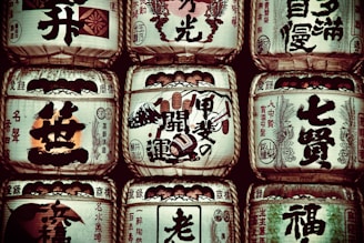Several traditional sake barrels are stacked in a symmetrical arrangement. Each barrel is adorned with Japanese calligraphy and symbols, highlighting intricate designs and various insignias representative of sake breweries.