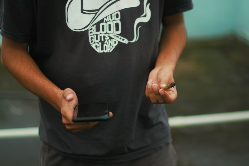 homme en noir et blanc ras du cou t-shirt tenant un smartphone noir