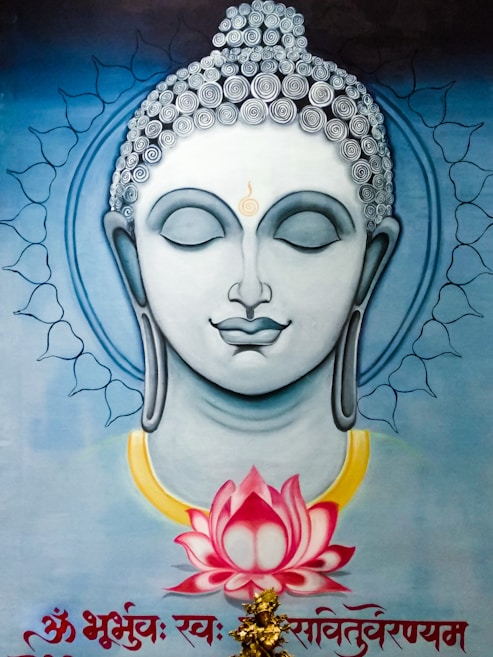 A serene and artistic depiction of a spiritual figure with closed eyes and a peaceful expression. The detailed hair is adorned with spiral patterns, and a subtle golden aura encircles the head, adding to the ethereal quality. Below, a vibrant pink lotus flower is depicted, surrounded by calm blue tones. Intricate designs and inscriptions in a script are present at the bottom of the image.