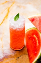 Bright red watermelon juice in a glass with watermelon slices beside it