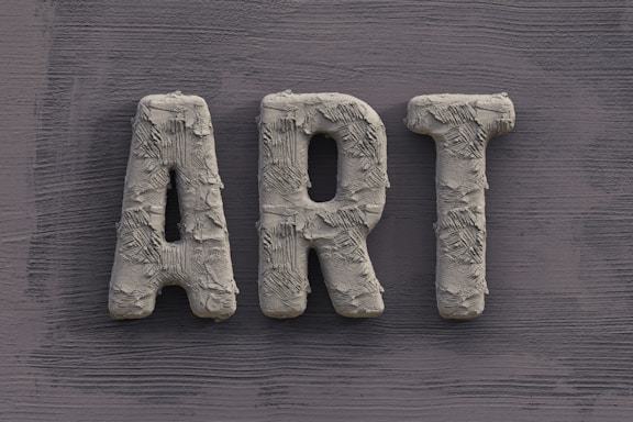 The word 'ART' is carved in a textured, concrete-like material, with rough, brush-stroke patterns covering the surface. It is set against a slate grey, wooden textured background.
