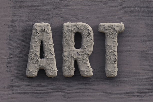The word 'ART' is carved in a textured, concrete-like material, with rough, brush-stroke patterns covering the surface. It is set against a slate grey, wooden textured background.