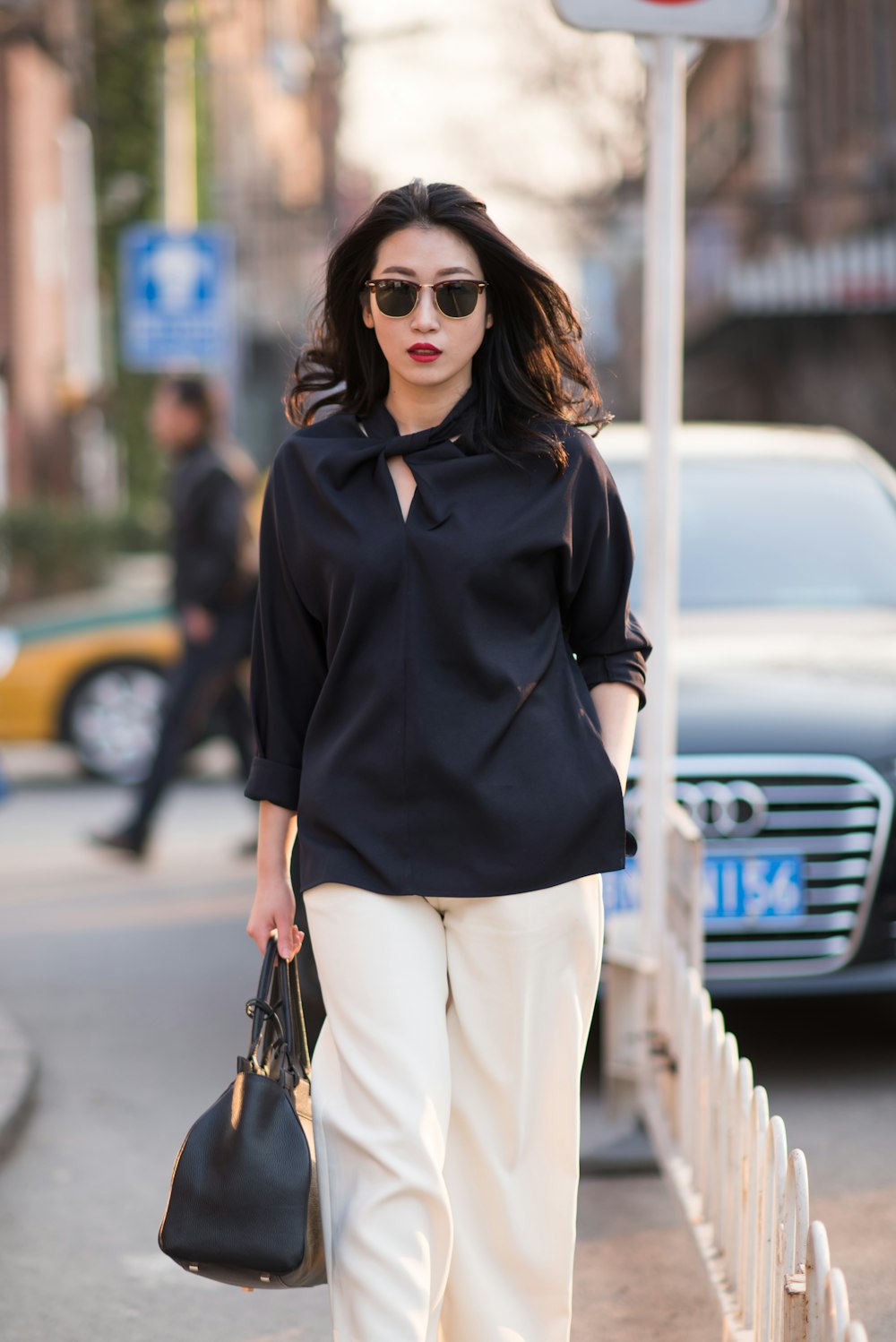 woman in black polo shirt and white pants wearing black sunglasses standing on road during daytime