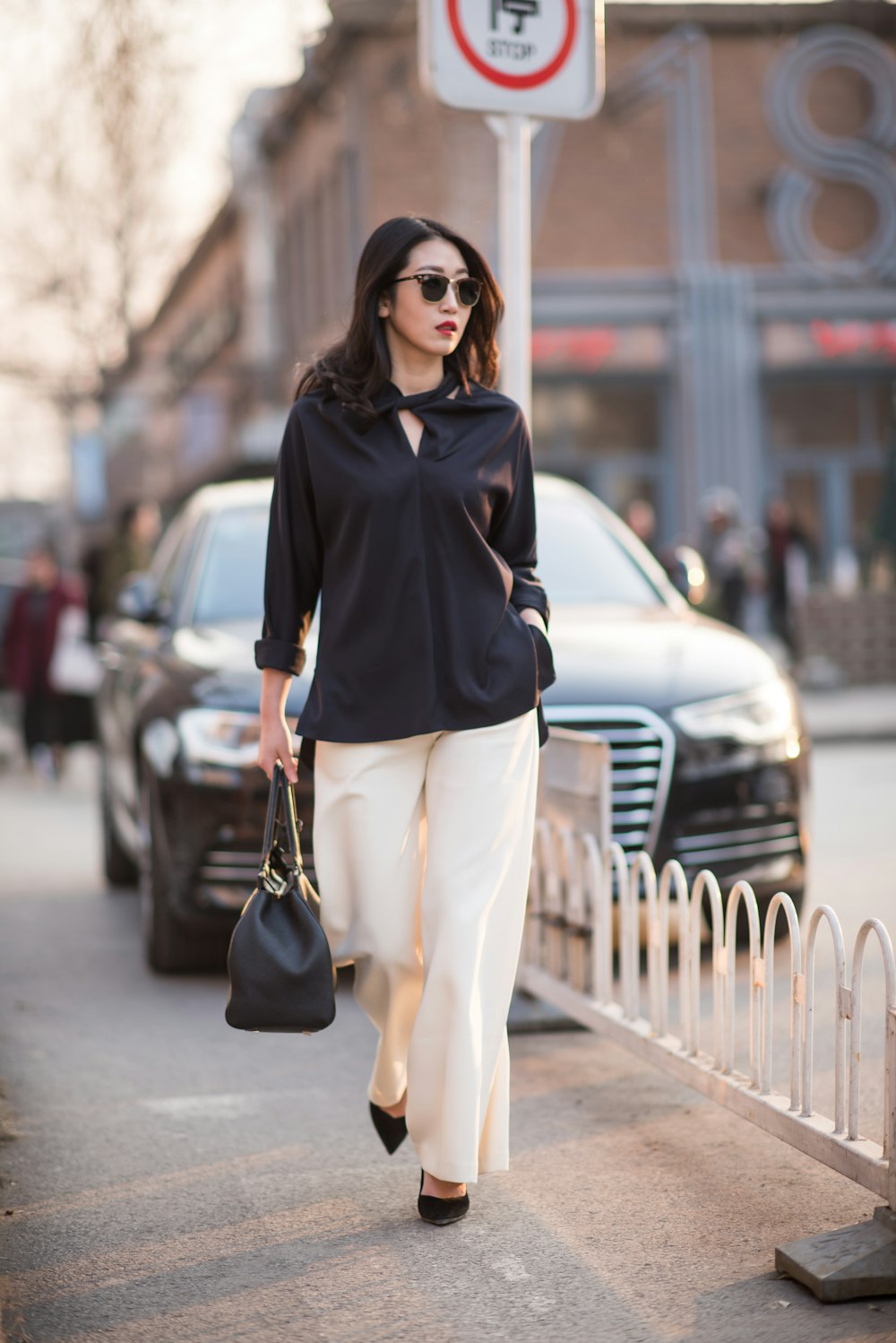 woman in black long sleeve shirt and white pants standing on sidewalk during daytime