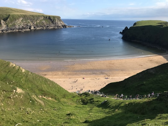 green grass covered mountain beside body of water during daytime in Donegal Ireland