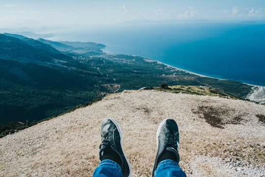 person in blue denim jeans and gray hiking shoes sitting on brown rock mountain during daytime in Llogara National Park Albania