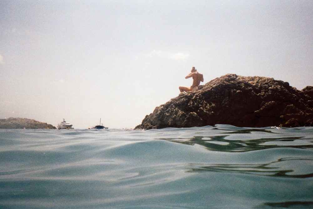 woman in white shirt sitting on rock in the middle of water