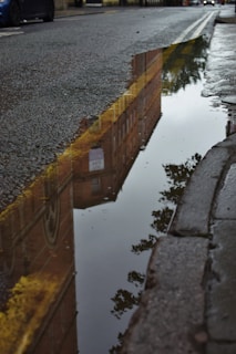 A large pothole filled with rainwater reflecting nearby buildings on a residential road