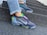 A pair of colorful, modern sneakers with multi-colored detailing and transparent soles is worn on a person's feet. The sneakers feature a prominent brand logo and are paired with light blue jeans with frayed hems. The person is standing on a set of rough-textured, concrete steps, suggesting an urban environment.
