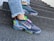 A pair of colorful, modern sneakers with multi-colored detailing and transparent soles is worn on a person's feet. The sneakers feature a prominent brand logo and are paired with light blue jeans with frayed hems. The person is standing on a set of rough-textured, concrete steps, suggesting an urban environment.