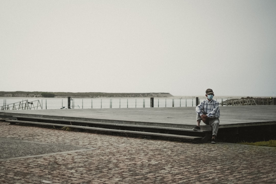 man in blue jacket and black pants sitting on bench