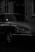 A cinematic shot of a vintage car parked under flickering street lamps.