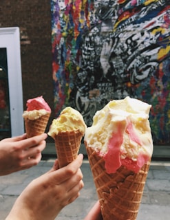 A group of friends laughing together, each holding colorful ice cream cones on a sunny day outside the shop.
