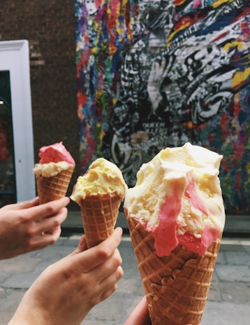 A group of friends laughing together, each holding colorful ice cream cones on a sunny day outside the shop.