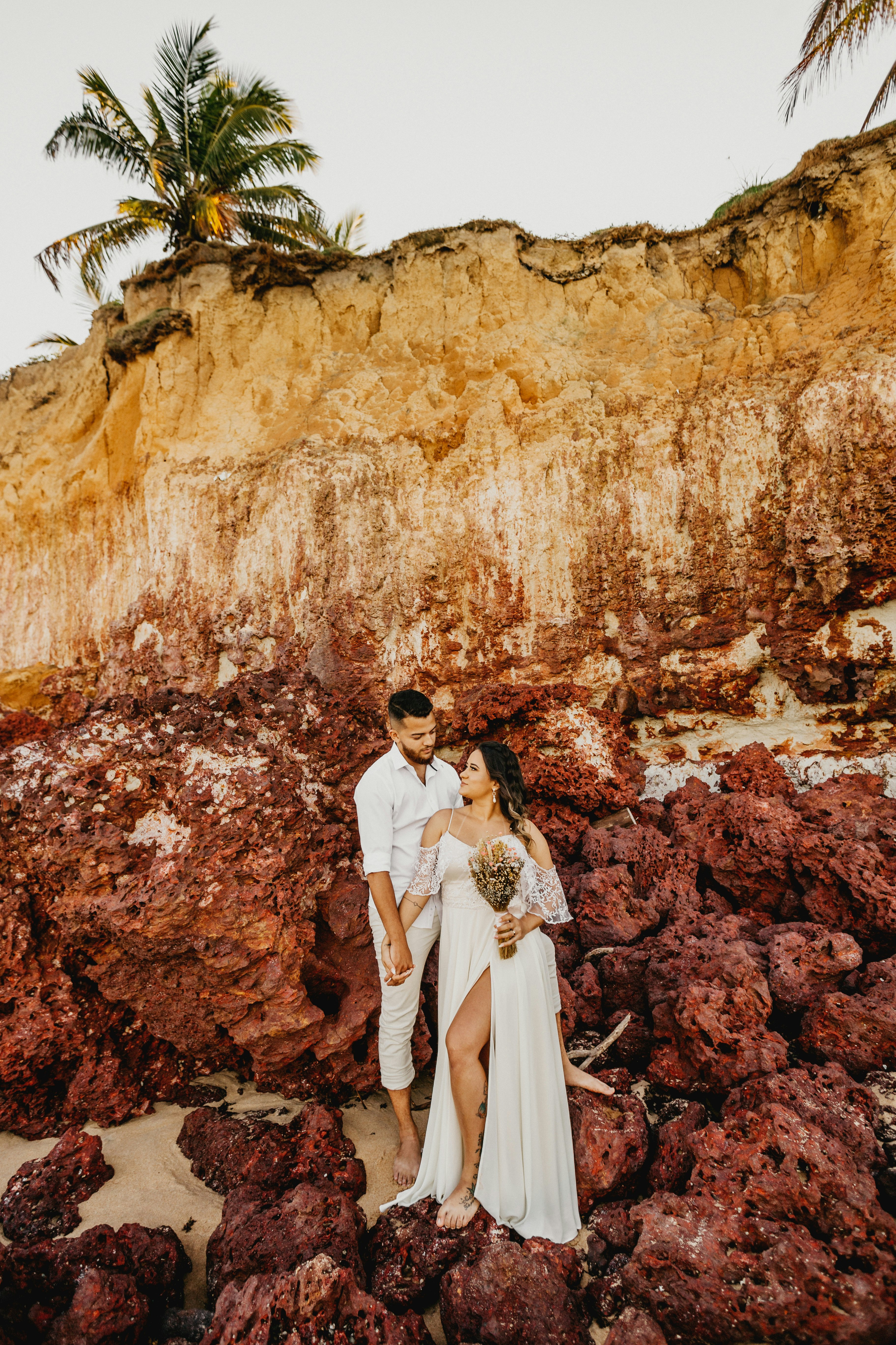 man and woman in white wedding dress standing in front of brown rock formation during daytime