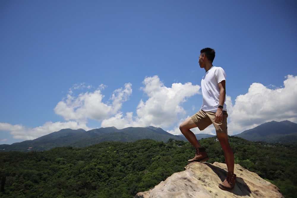 man in white t-shirt and brown shorts standing on brown rock during daytime