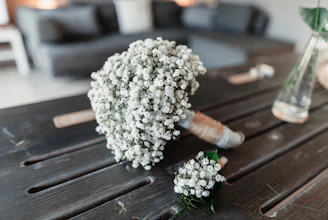 A softly lit bridal bouquet in white and baby blue hues resting on a rustic wooden table.