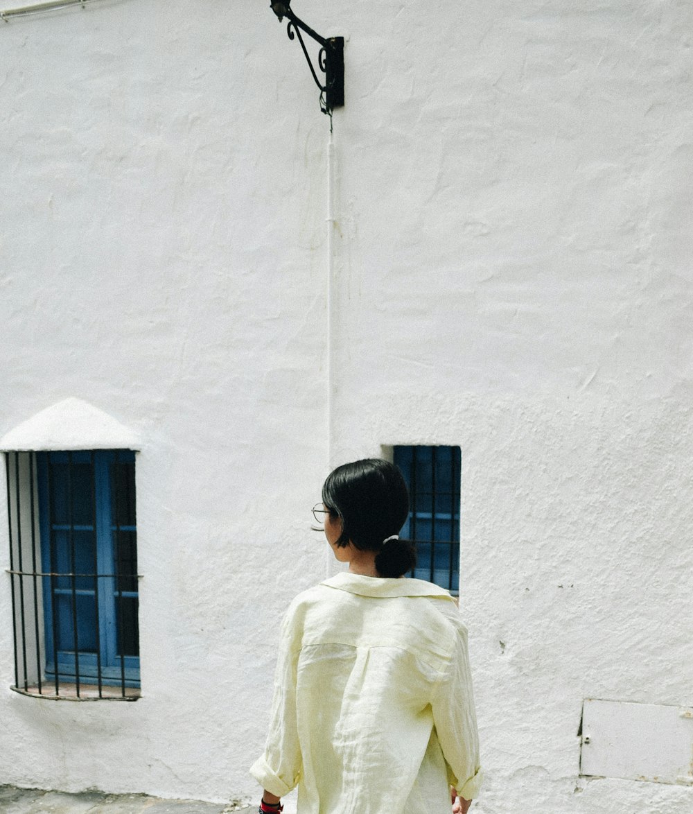 man in beige dress shirt standing in front of white concrete wall