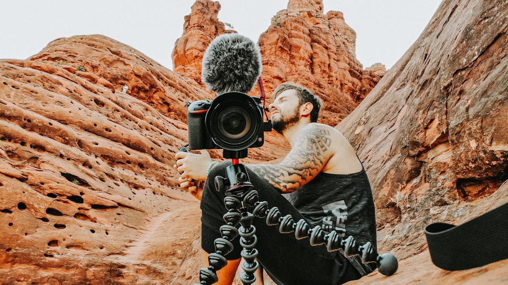 man in black tank top holding black nikon dslr camera