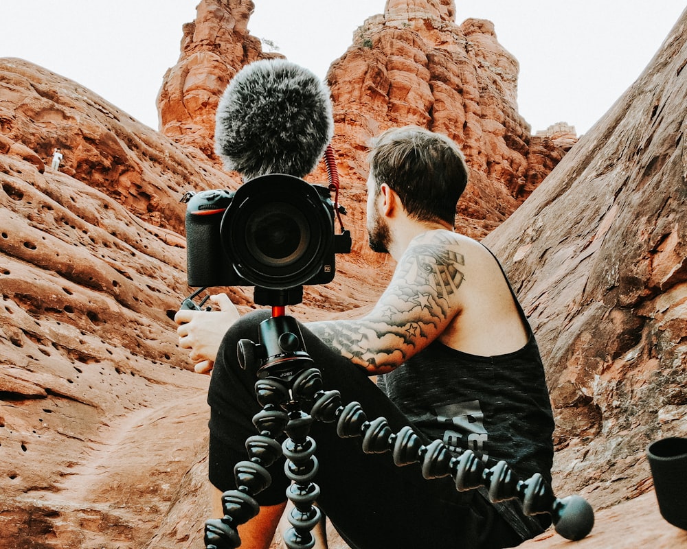 man in black tank top holding black dslr camera