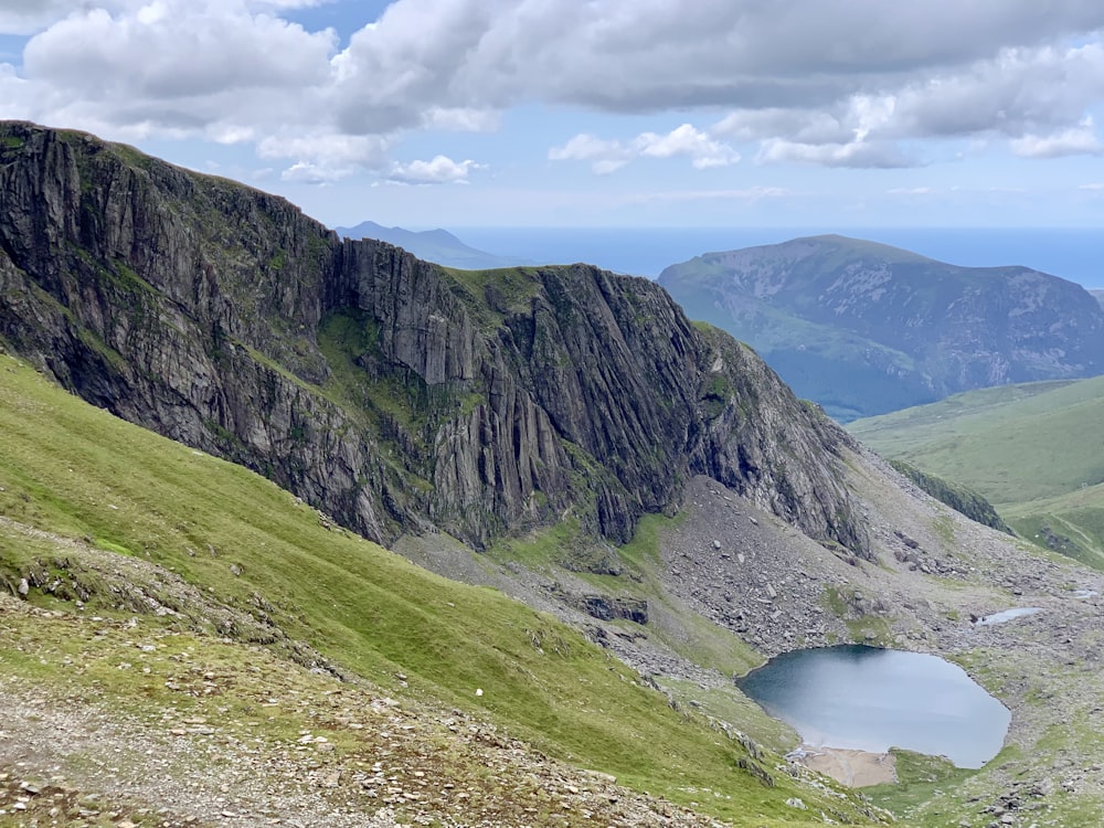 green and brown mountain beside lake under white clouds and blue sky during daytime