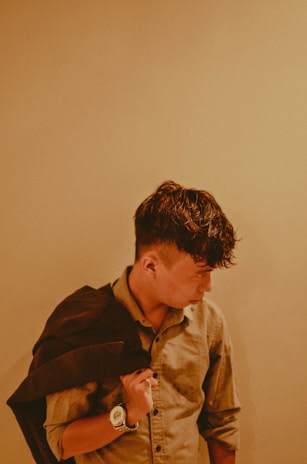 A person in a casual shirt is holding a dark jacket over their shoulder, looking down to their left. The image has a warm tone, with soft lighting that creates a relaxed atmosphere.