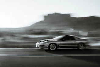 Low-angle shot of a sleek performance car speeding past a highway camera, emphasizing textured asphalt and heat haze.