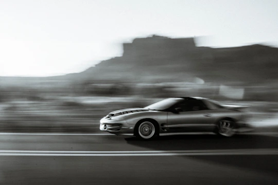 Low-angle shot of a sleek performance car blurring past a highway camera, heat haze rising from the exhaust over textured asphalt.