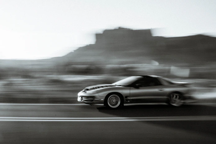 Low-angle shot of a sleek performance car speeding past a highway camera, emphasizing textured asphalt and heat haze.