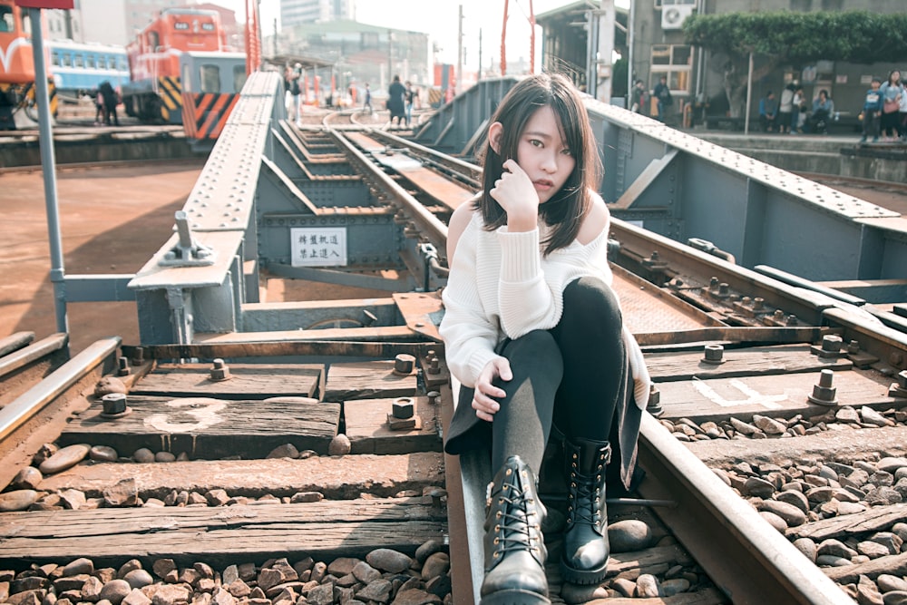 woman in white long sleeve shirt and black pants sitting on brown wooden frame during daytime