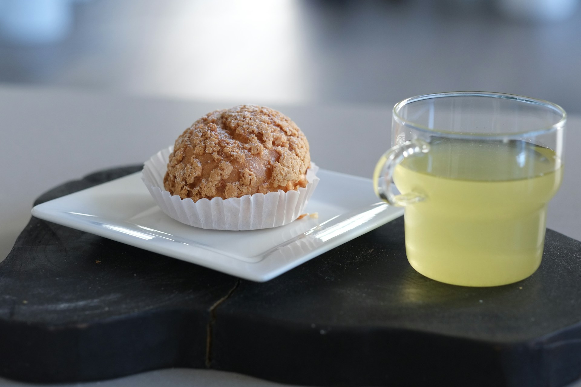 A freshly baked cream puff with golden, flaky pastry and a generous swirl of whipped cream, resting on a vintage china plate.