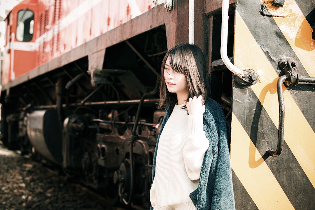 woman in white shirt and blue denim jacket standing beside train