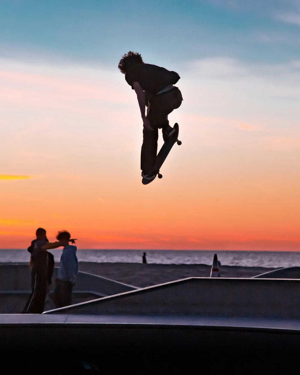 man in black shorts and woman in white shirt jumping on the beach during sunset