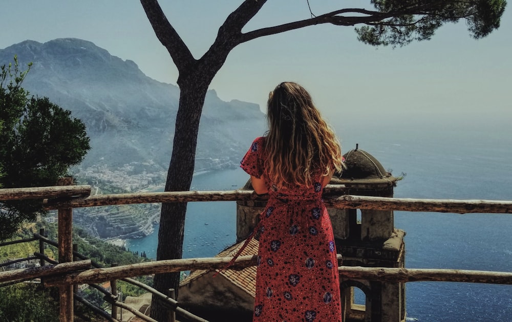 woman in red and black floral dress standing near brown wooden railings during daytime