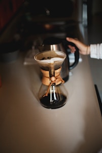 A cozy home kitchen with a barista carefully pouring coffee from a Chemex, surrounded by Bodhi Beans coffee bags and brewing tools.