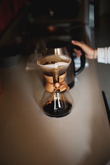 A cozy home kitchen with a barista carefully pouring coffee from a Chemex, surrounded by Bodhi Beans coffee bags and brewing tools.