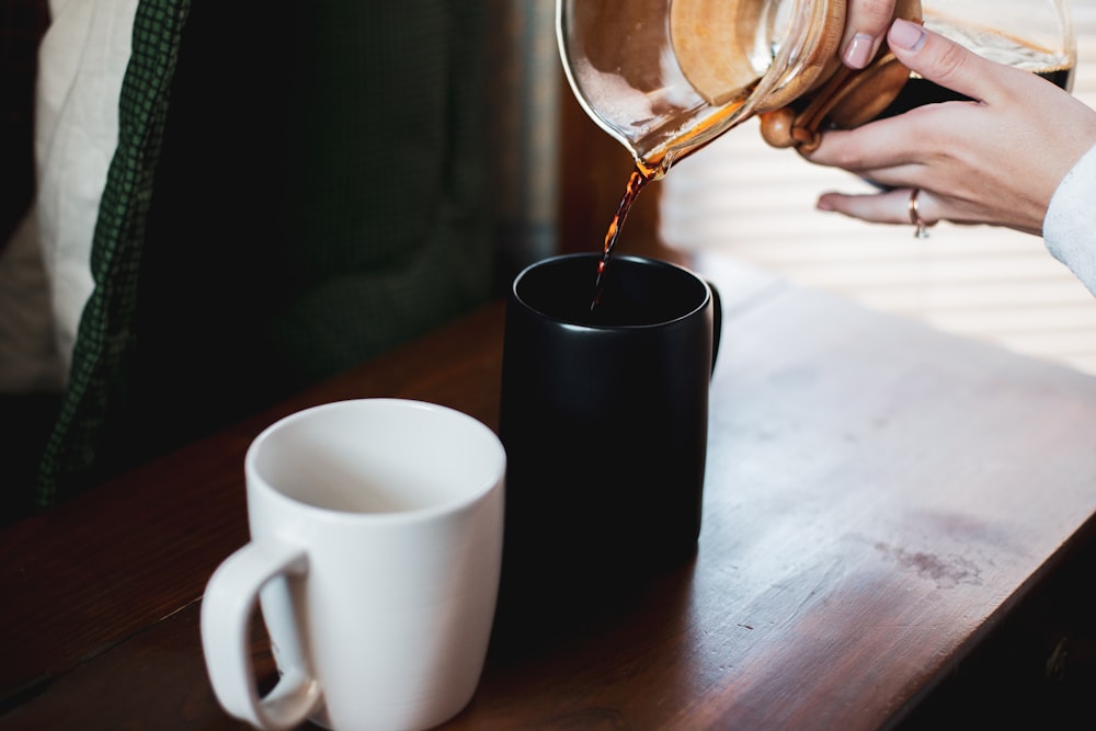 person pouring water on black ceramic mug