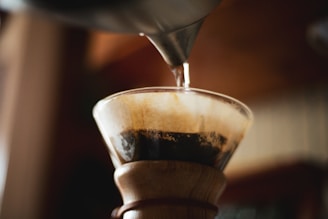 A close-up shot of freshly brewed coffee dripping from a pour-over coffee maker into a glass carafe.