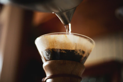 A close-up of freshly brewed coffee dripping from a pour-over cone into a glass carafe on a wooden table.
