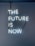 A neon sign with the phrase 'THE FUTURE IS NOW' mounted on a dark blue wall. The letters are glowing in a bright white light, with visible wires connecting them.