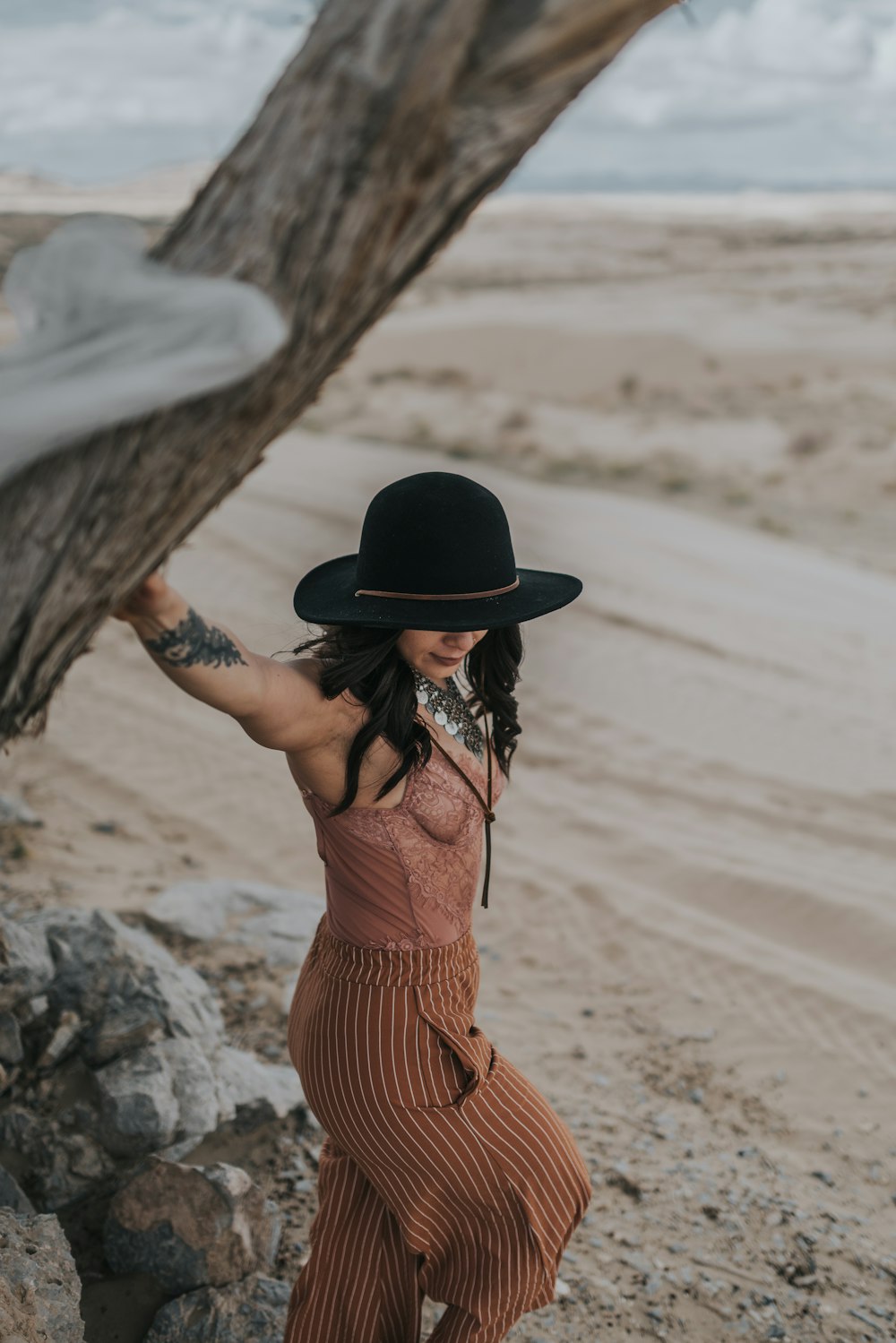 Mujer con vestido de rayas marrones y negras con sombrero negro de pie sobre arena marrón durante el día