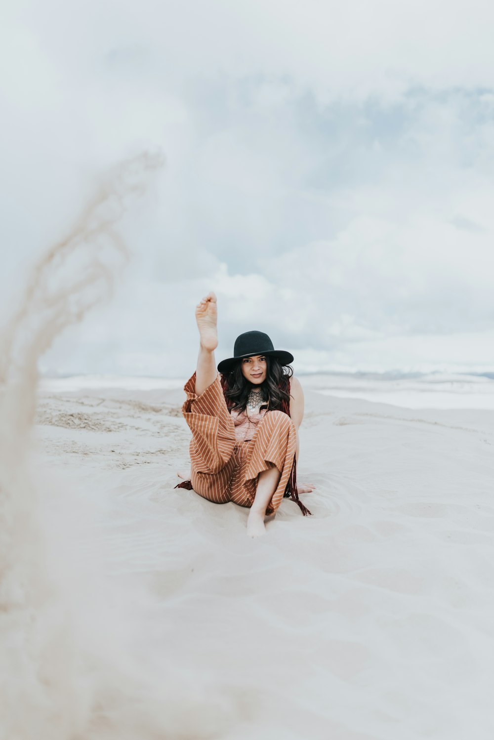 woman in black hat and brown and white stripe shirt sitting on white sand beach during