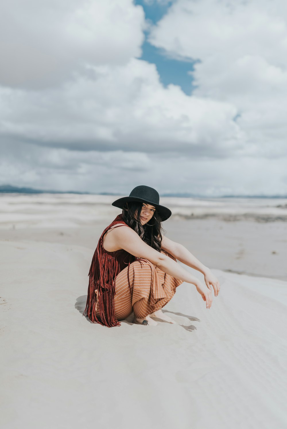 woman in brown and black plaid dress shirt and black fedora hat sitting on beach during