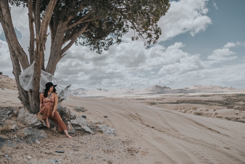 woman in black bikini lying on sand near tree during daytime