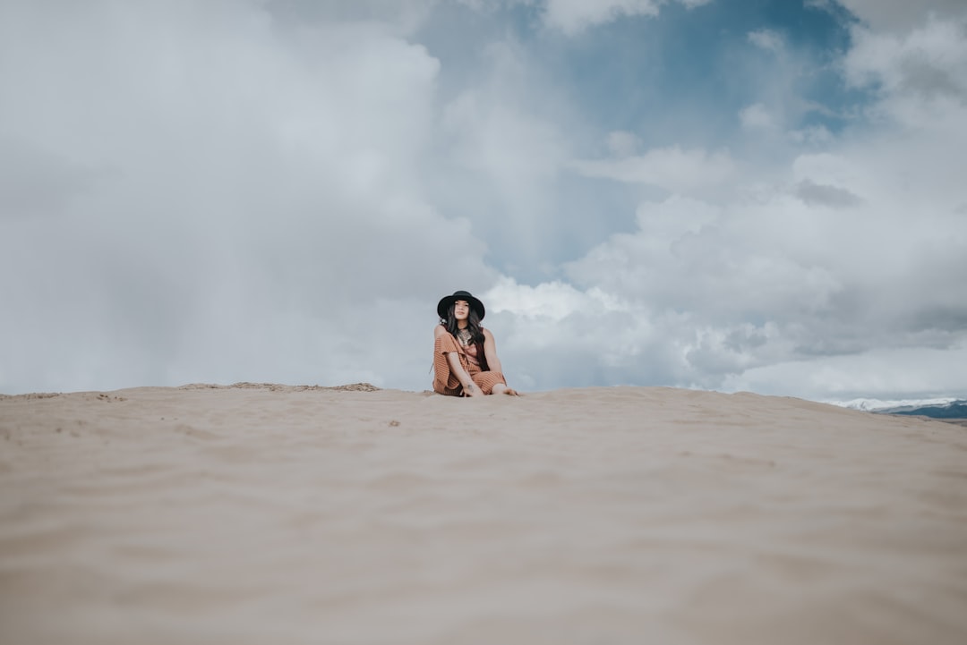 woman in black bikini lying on brown sand under white clouds during daytime