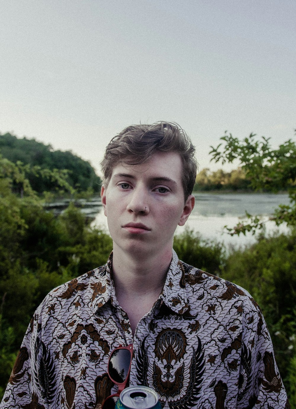 man in black and white floral button up shirt standing near green trees during daytime