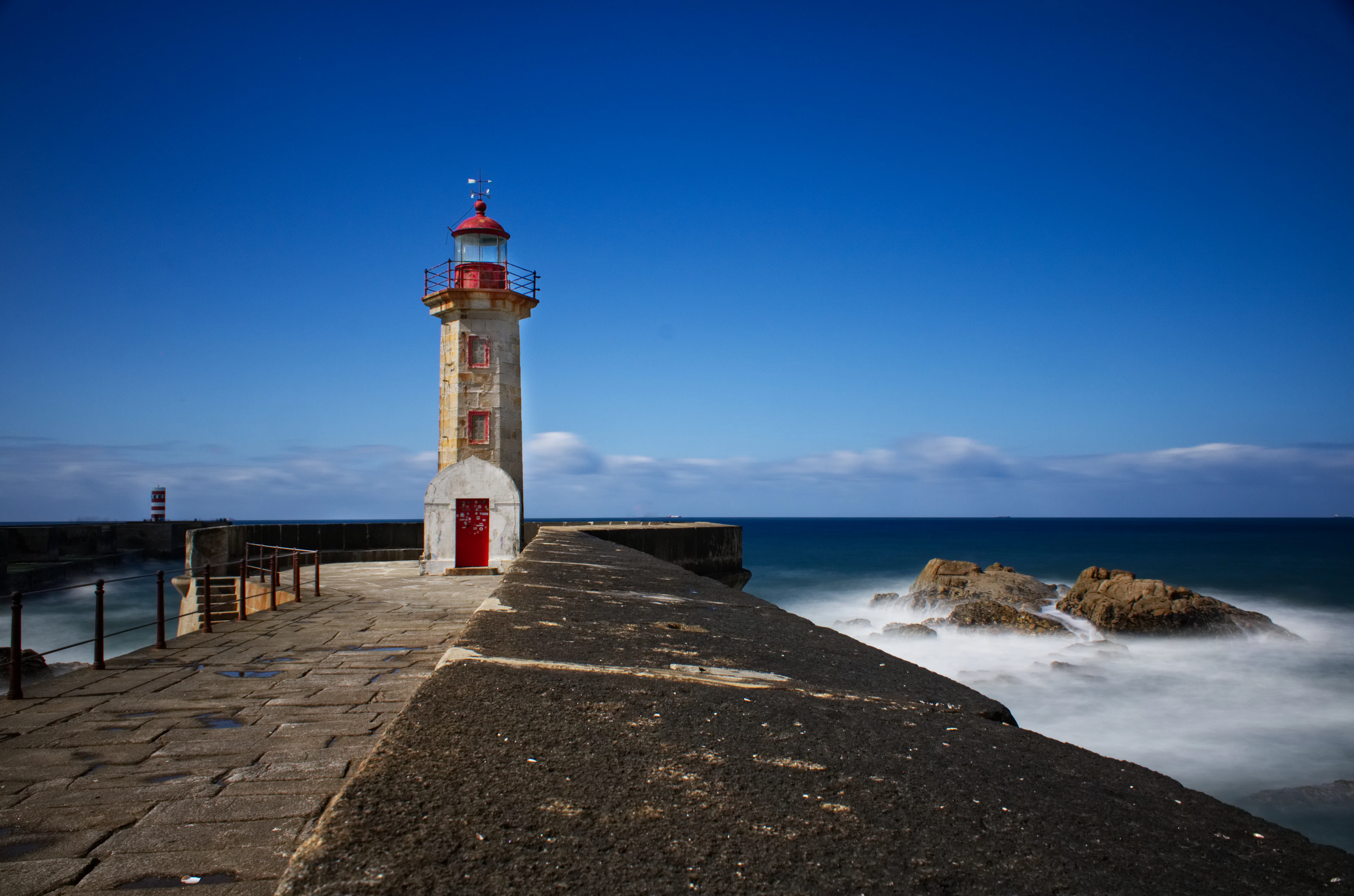 The red-and-white Felgueiras lighthouse stands on a stone pier above the Atlantic surf.