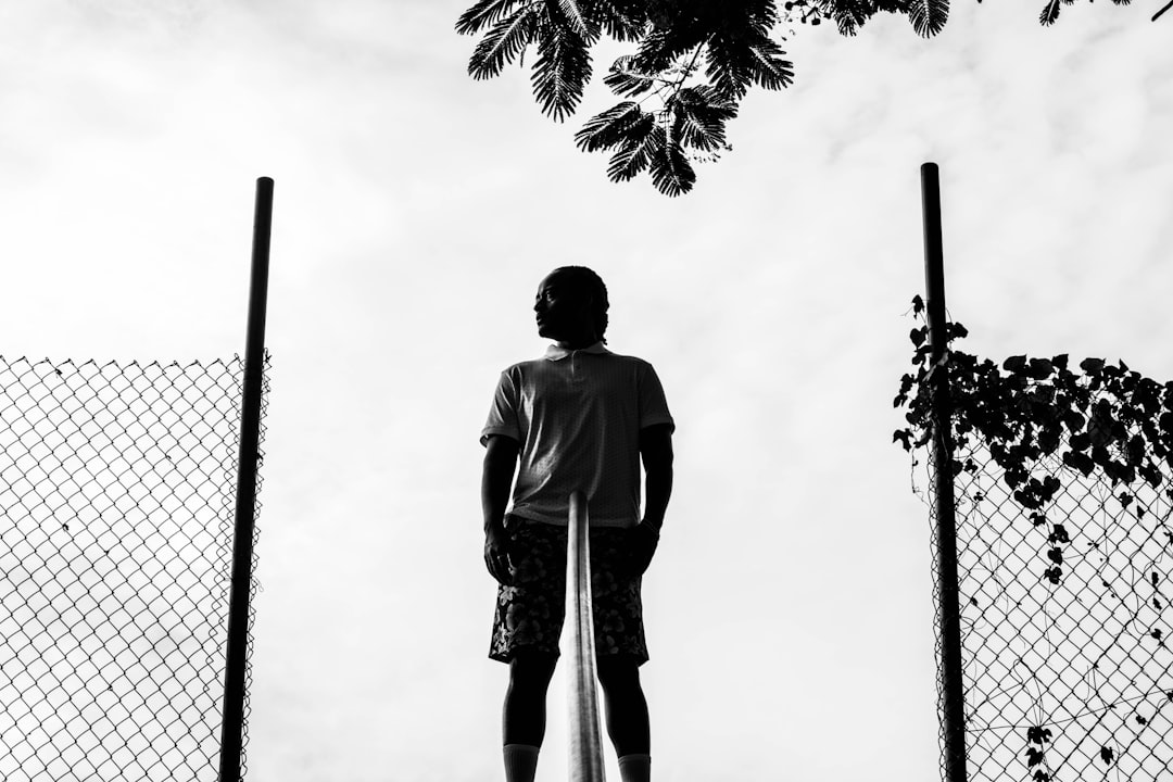 man in white t-shirt and black shorts standing near palm tree