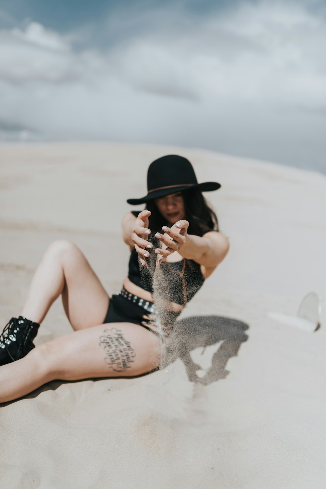 woman in black and white dress wearing black hat sitting on white sand during daytime