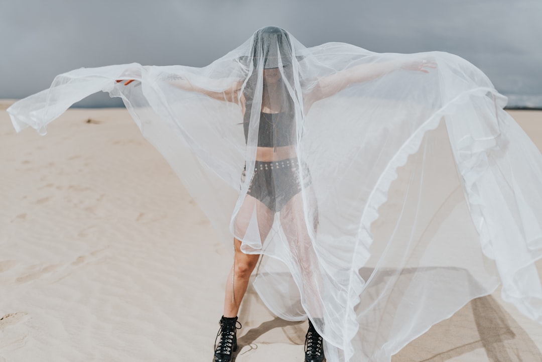 woman in white wedding dress and black leather boots standing on white sand